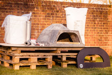 Load image into Gallery viewer, All parts of a DIY pizza oven kit placed ontop of pallets in front of a brick wall
